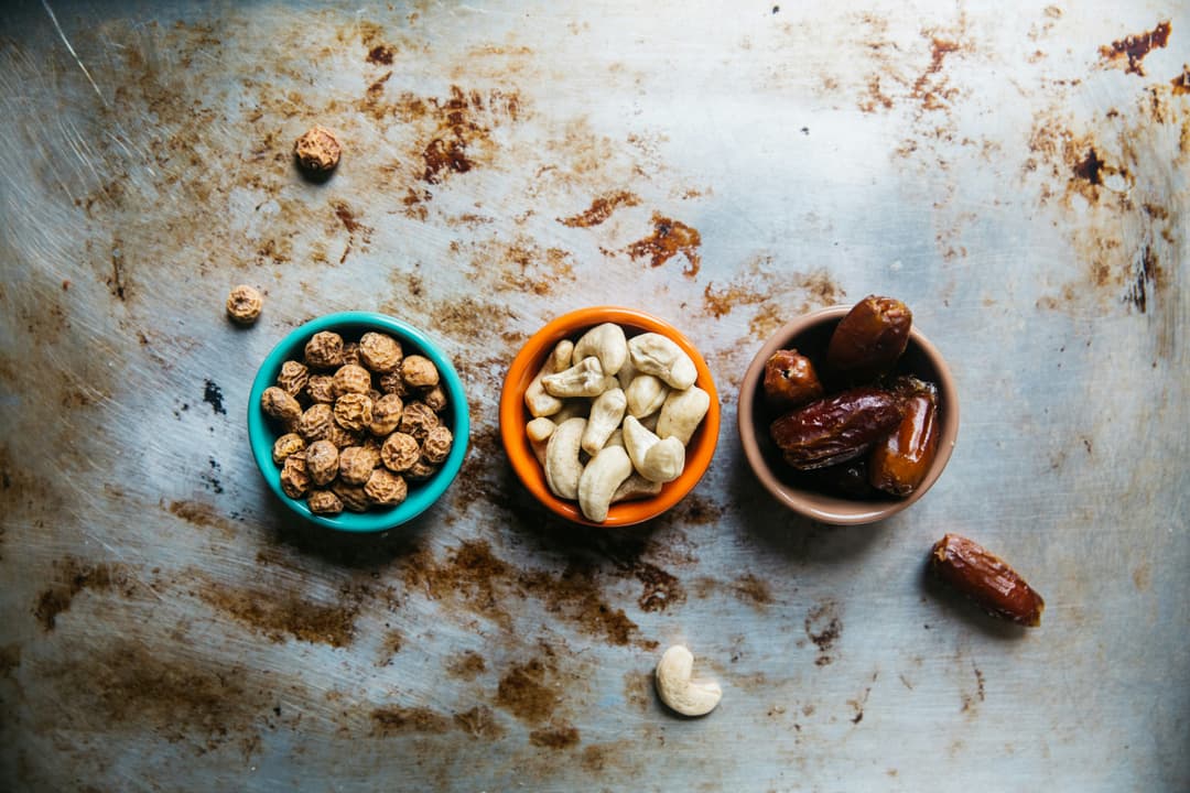 Top view of three bowls filled with tiger nuts, cashew nuts, and dates